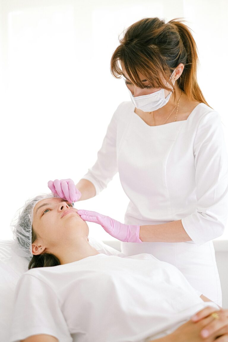 A beautician performs a cosmetic treatment on a woman in a clinical setting.
